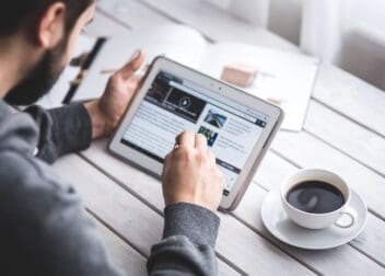 man at table reading a webzine, e-zine, web magazine, online magazine, digital magazine, internet magazine, cybermagazine with a cup of coffee